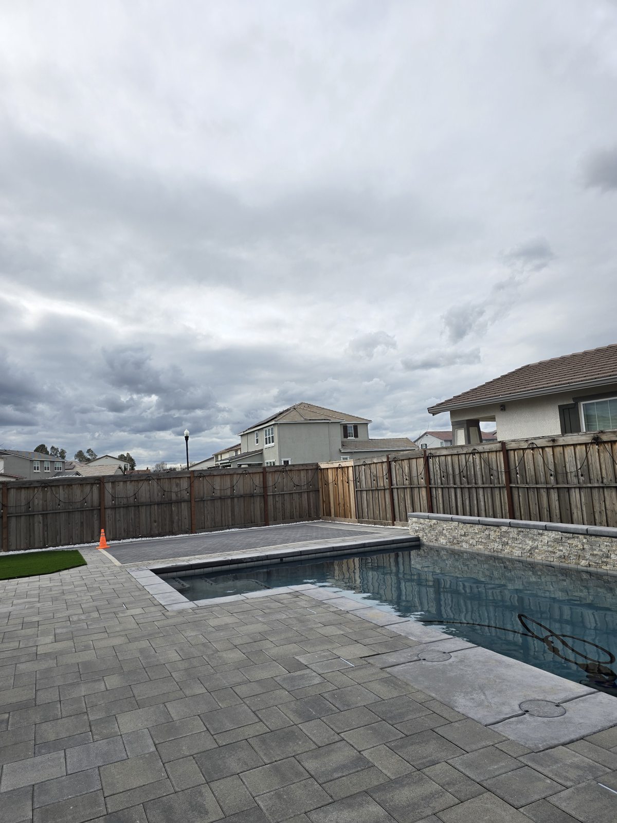A generous paver terrace extends alongside the pool and raised stone wall.