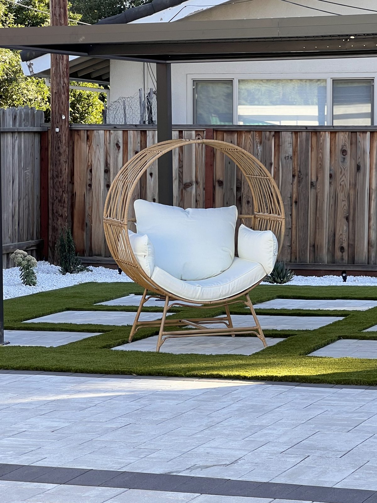 Large paving shapes and green accents frame a suspended outdoor chair.