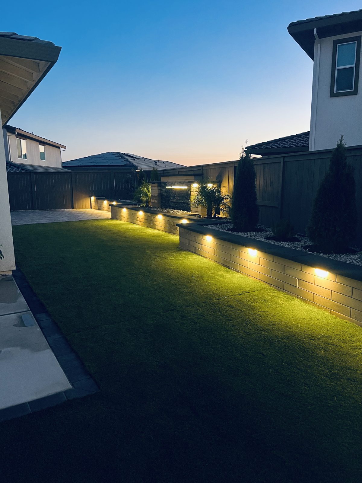 Soft lighting traces the lawn and boundary wall for a welcoming evening atmosphere.