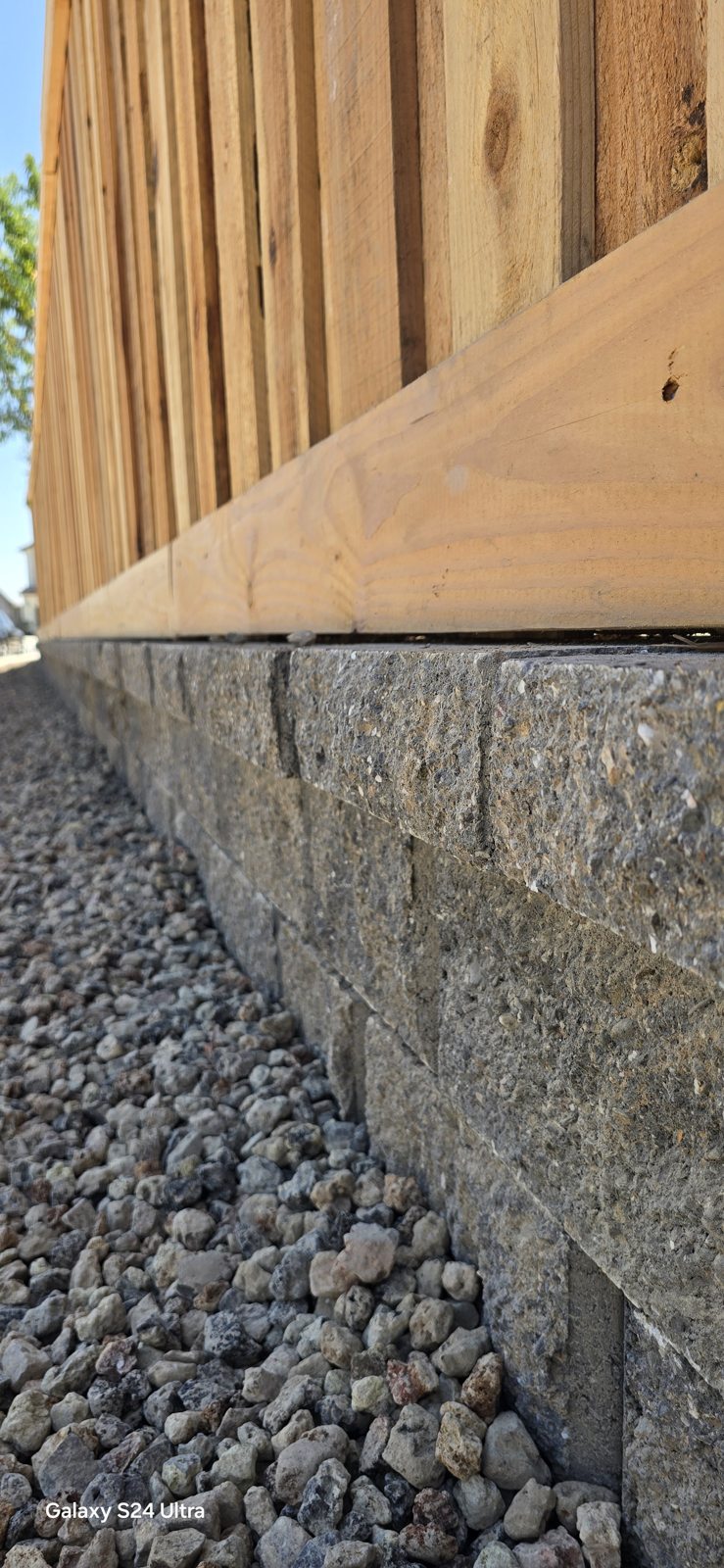 Stone-facing and pale decorative rock create a clean finish beneath the wood fence.