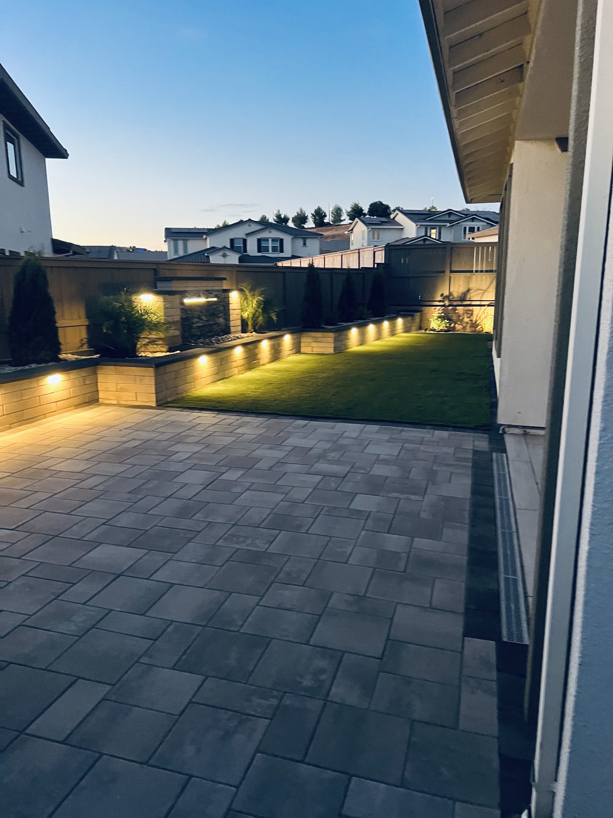 An evening view reveals the contrast between textured pavers and a glowing garden edge.