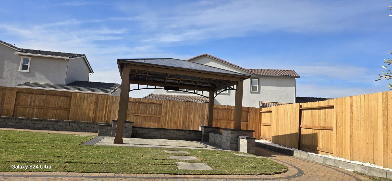 A curved wall and paved approach connect the lawn with a sheltered garden structure.