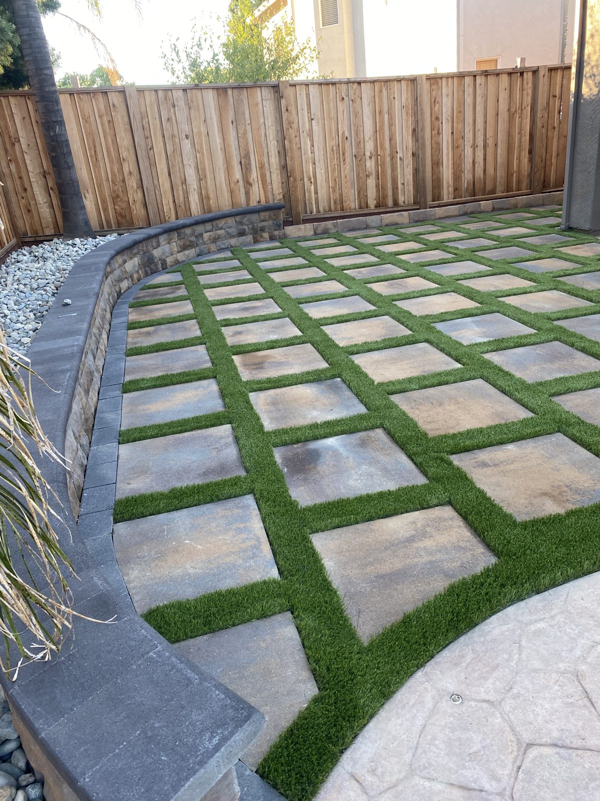 A sequence of pale stepping surfaces gives the green side yard a rhythmic pattern.