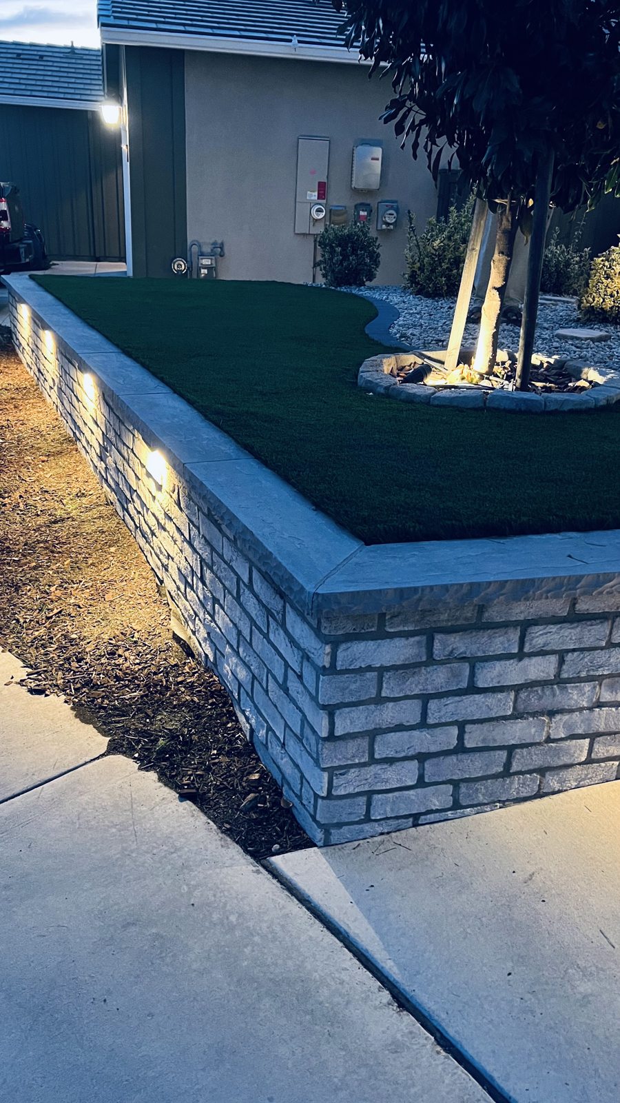 A masonry corner detail combines a crisp cap, green lawn and subtle lighting.