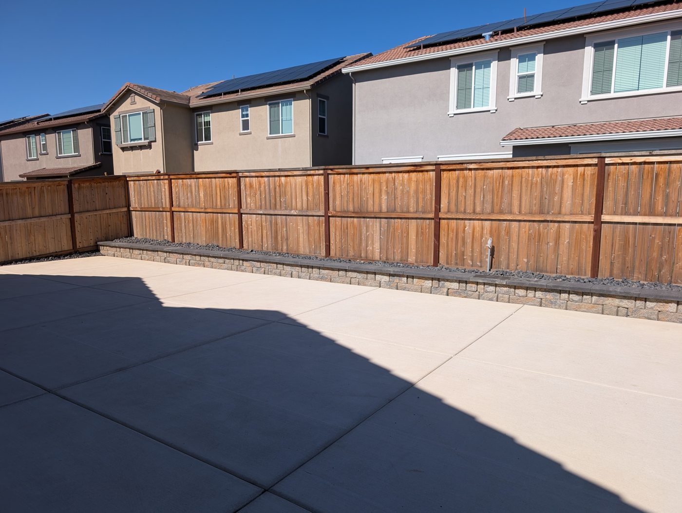 A long timber fence gives the paved backyard a unified perimeter.
