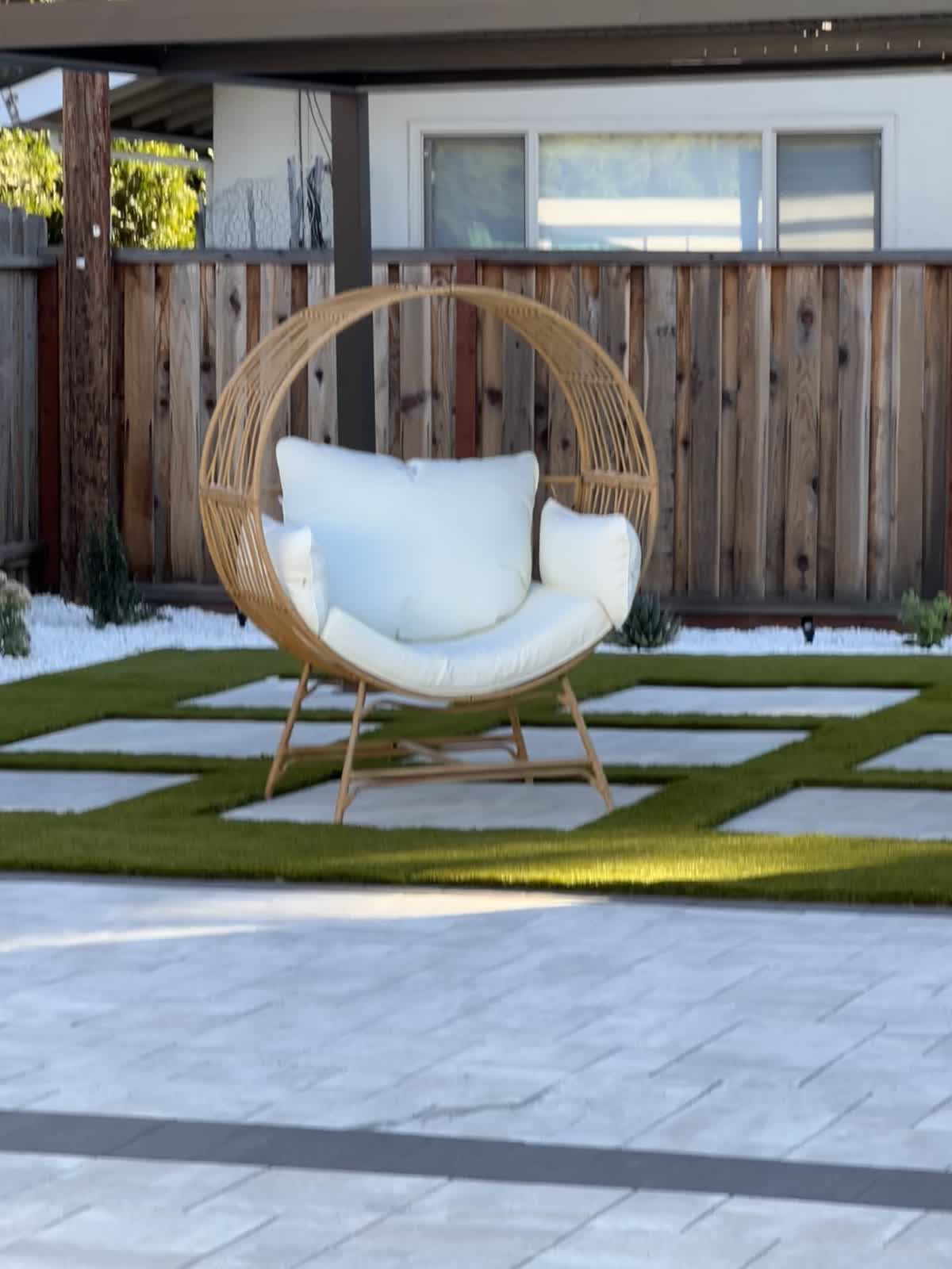 A suspended garden chair sits within a crisp pattern of green turf and pale paving.
