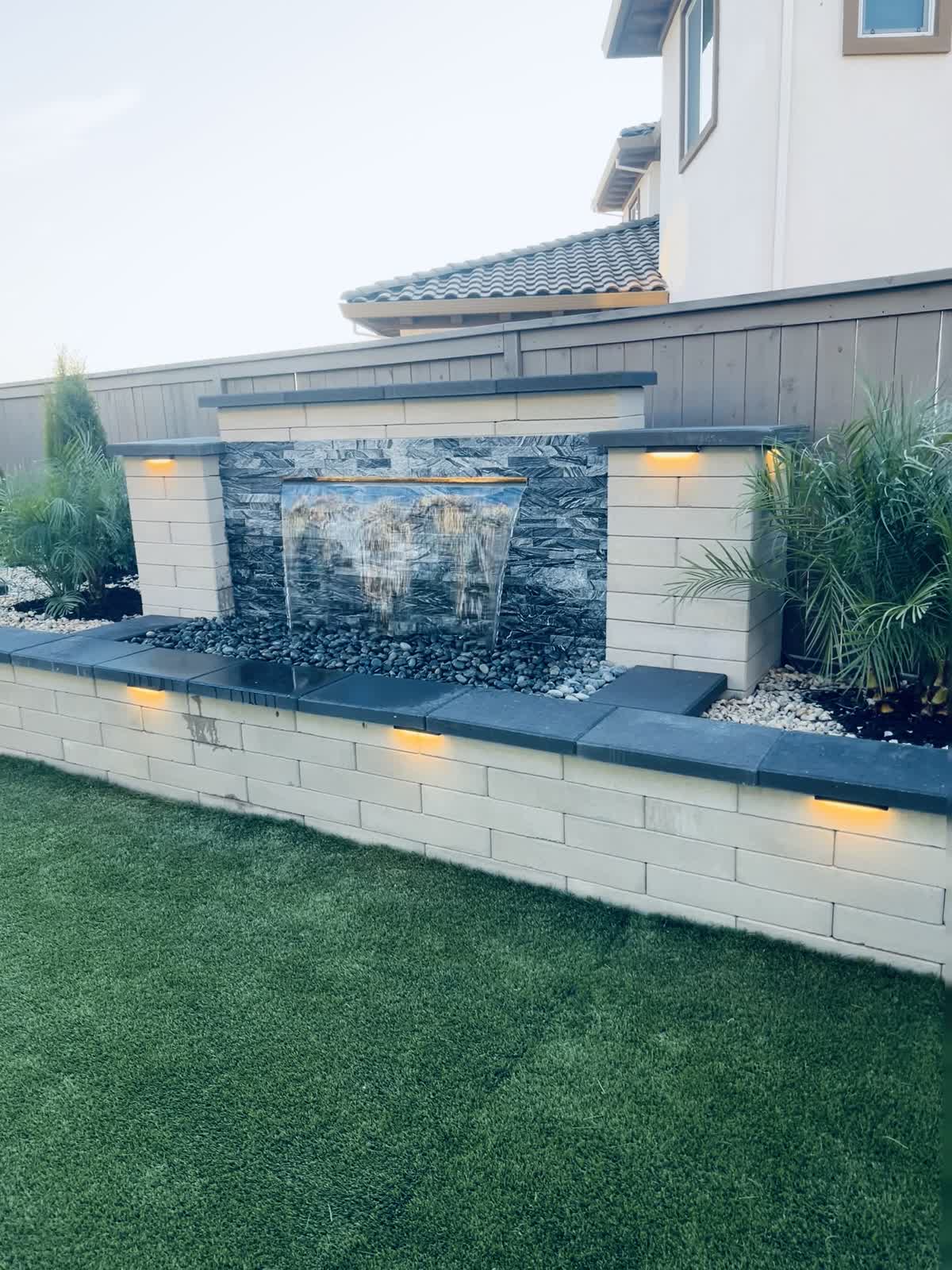 Falling water animates the stone wall and becomes a focal point beside the lawn.