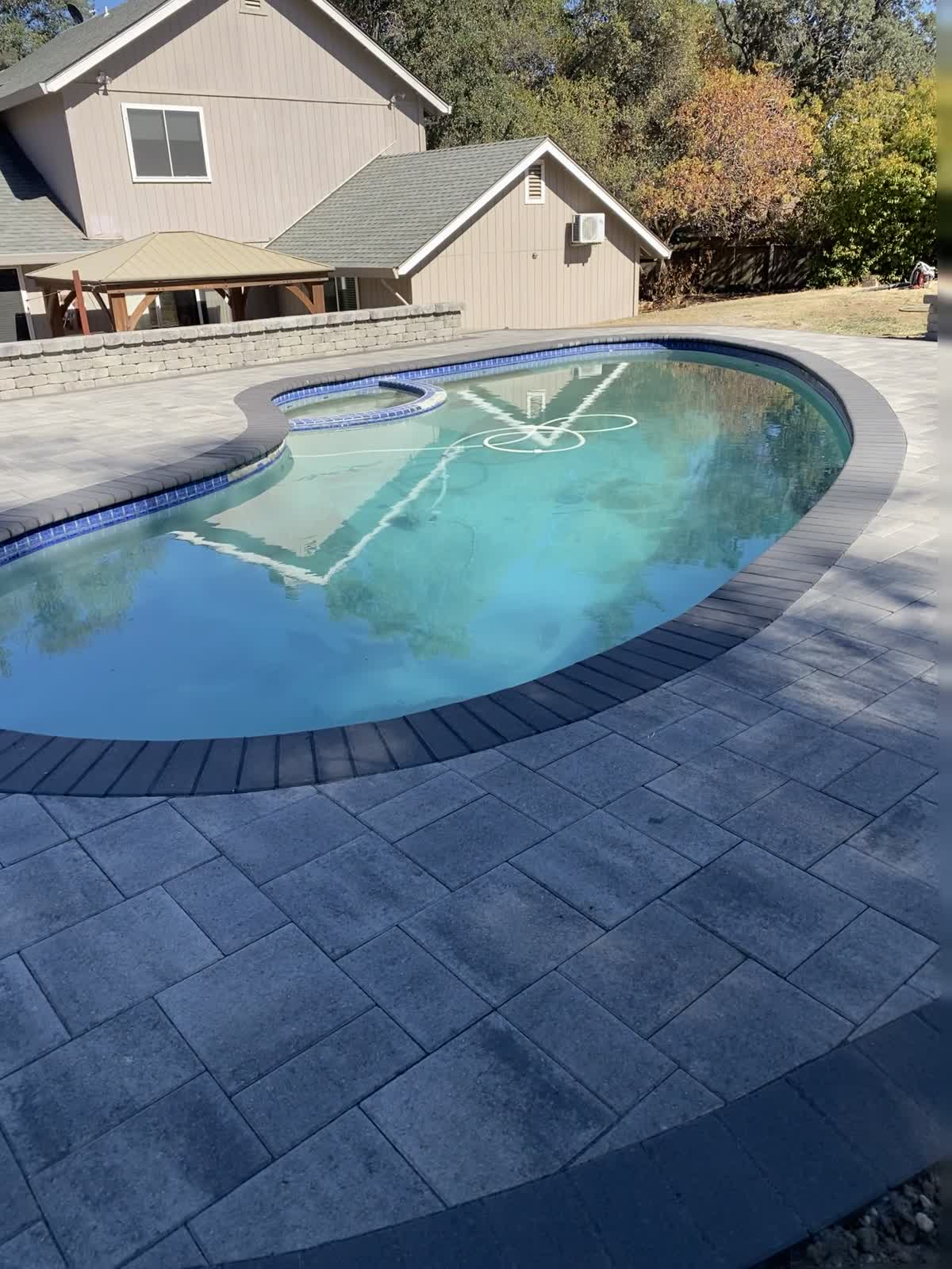 A rounded pool is framed by textured gray paving and an open outdoor terrace.